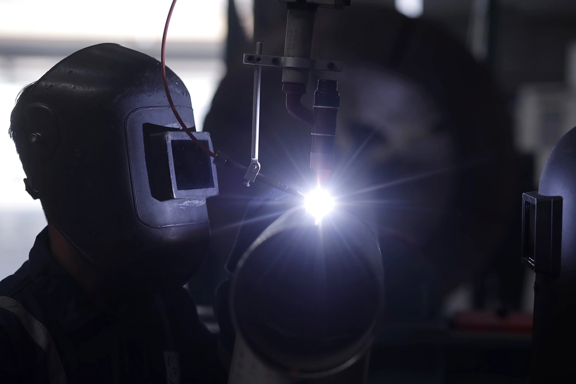Welder in a protective helmet watching a mechanised TIG weld on a pipe joint
